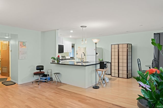 kitchen with white cabinetry, light wood-type flooring, kitchen peninsula, and decorative light fixtures