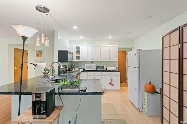 kitchen featuring black appliances, a kitchen bar, hanging light fixtures, light hardwood / wood-style floors, and white cabinets