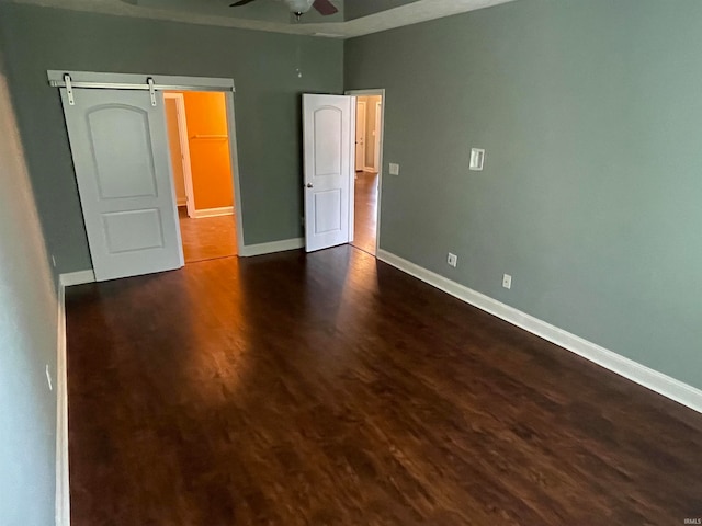 unfurnished bedroom featuring a barn door, dark hardwood / wood-style floors, and ceiling fan