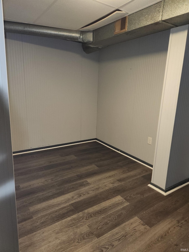 basement featuring a paneled ceiling and dark hardwood / wood-style floors