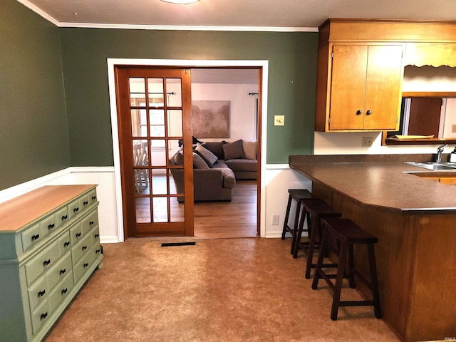 kitchen featuring a kitchen breakfast bar, sink, light colored carpet, and ornamental molding