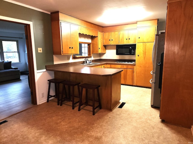 kitchen with stainless steel refrigerator, light carpet, a kitchen bar, sink, and kitchen peninsula