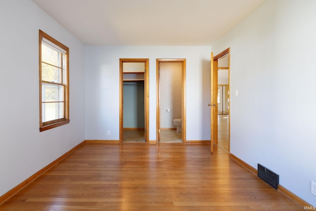 unfurnished bedroom featuring ensuite bath, wood-type flooring, and a walk in closet