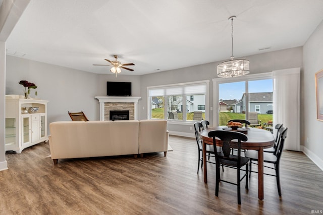 dining space featuring dark wood-type flooring, a fireplace, and ceiling fan with notable chandelier