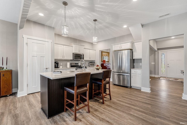 kitchen featuring stainless steel appliances, light hardwood / wood-style floors, white cabinetry, and a center island with sink