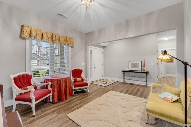 sitting room with hardwood / wood-style flooring, a textured ceiling, and a notable chandelier