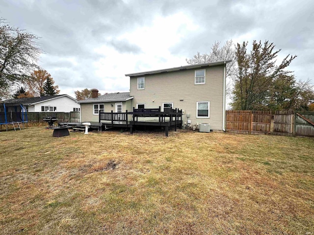 rear view of property with central AC unit, a trampoline, a deck, and a lawn