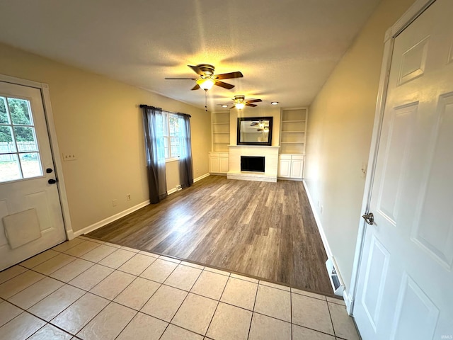 unfurnished living room with light tile patterned flooring, a wealth of natural light, a textured ceiling, and built in shelves