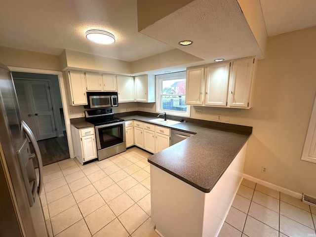 kitchen featuring white cabinetry, a textured ceiling, light tile patterned floors, kitchen peninsula, and stainless steel appliances