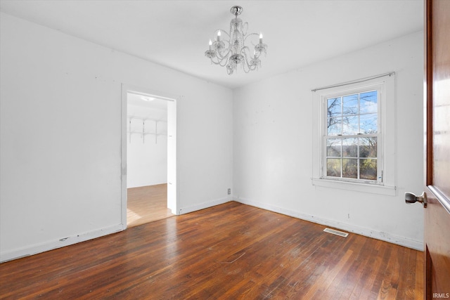 spare room with dark hardwood / wood-style flooring and a notable chandelier