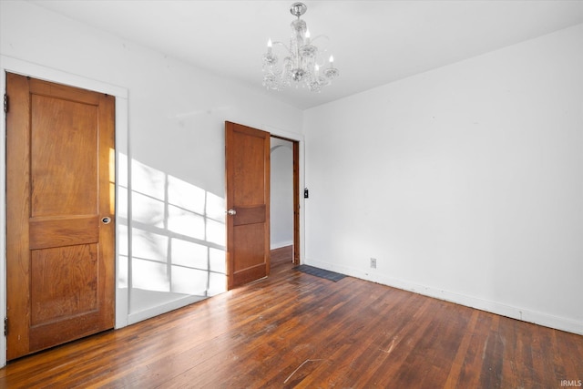 spare room with dark wood-type flooring and a notable chandelier