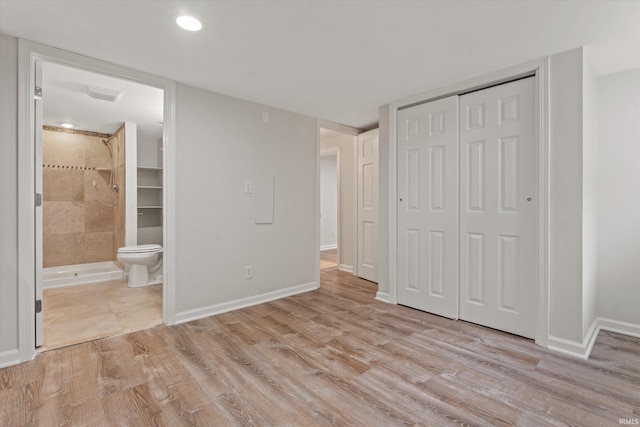 unfurnished bedroom featuring light wood-type flooring, ensuite bath, and a closet