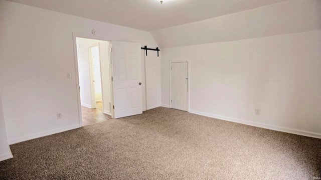 interior space featuring a barn door, vaulted ceiling, and carpet floors