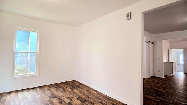 empty room featuring a barn door, dark hardwood / wood-style floors, and plenty of natural light