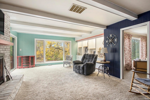 living area featuring beamed ceiling, carpet, a brick fireplace, and plenty of natural light