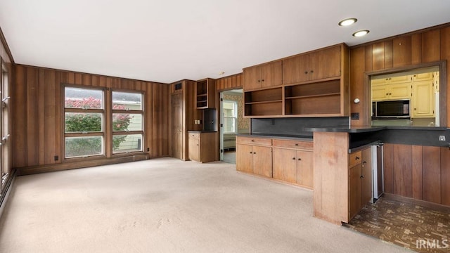 kitchen featuring kitchen peninsula, light colored carpet, and wood walls