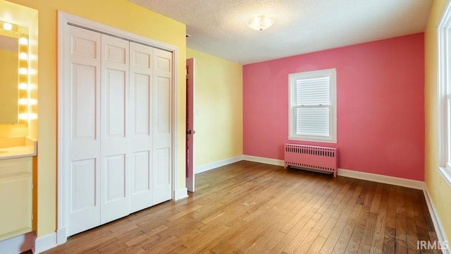 unfurnished bedroom featuring a closet, a textured ceiling, light wood-type flooring, and radiator