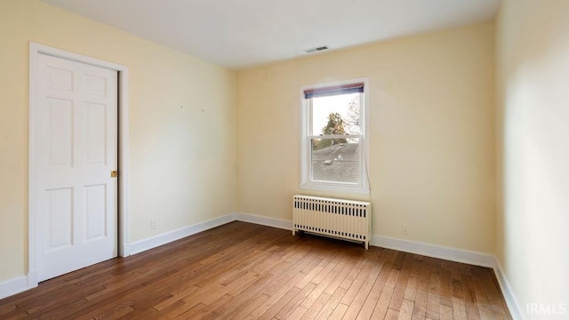 empty room with hardwood / wood-style floors and radiator heating unit