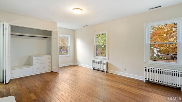 unfurnished bedroom featuring multiple windows, radiator heating unit, and a closet