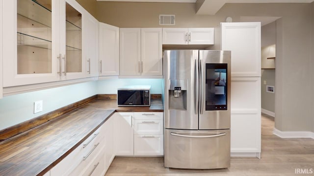 kitchen featuring white cabinetry, stainless steel fridge with ice dispenser, light hardwood / wood-style floors, and wood counters