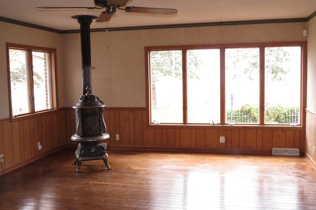 unfurnished sunroom featuring ceiling fan, plenty of natural light, and a wood stove