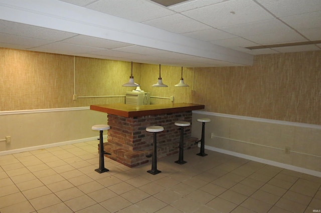 bar featuring wooden walls, a drop ceiling, decorative light fixtures, and tile patterned flooring