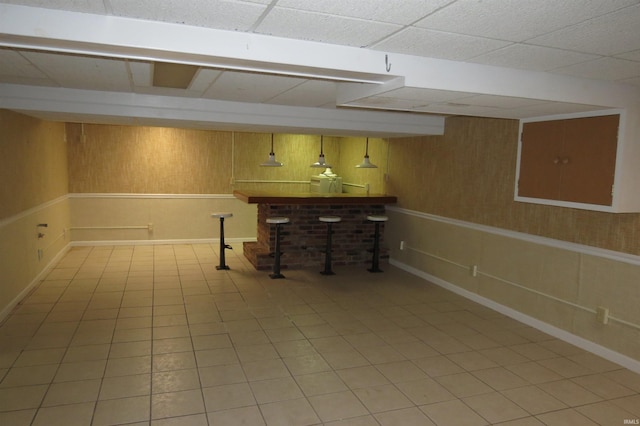 basement with bar, wooden walls, tile patterned floors, and a paneled ceiling