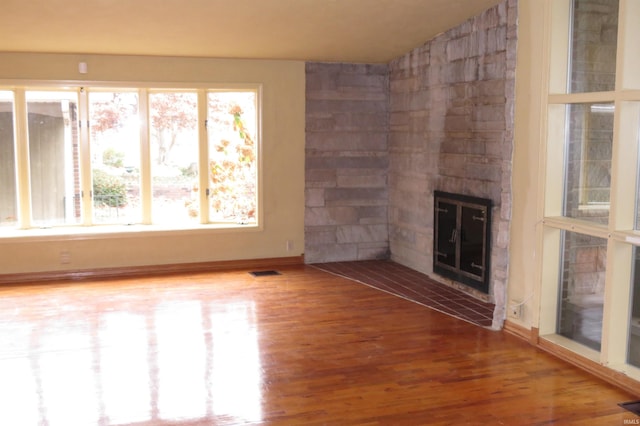 unfurnished living room featuring a stone fireplace, hardwood / wood-style floors, a healthy amount of sunlight, and vaulted ceiling