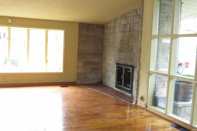 unfurnished living room with wood-type flooring, plenty of natural light, a stone fireplace, and lofted ceiling