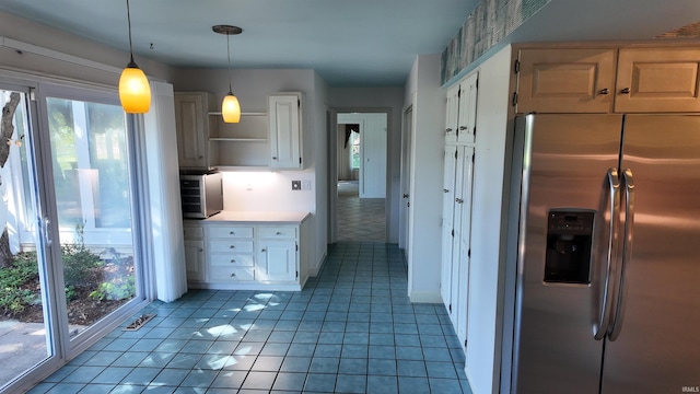 kitchen featuring decorative light fixtures, stainless steel fridge, light tile patterned flooring, and white cabinetry