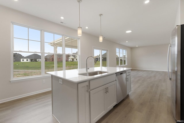 kitchen featuring stainless steel appliances, light wood-type flooring, hanging light fixtures, sink, and a kitchen island with sink