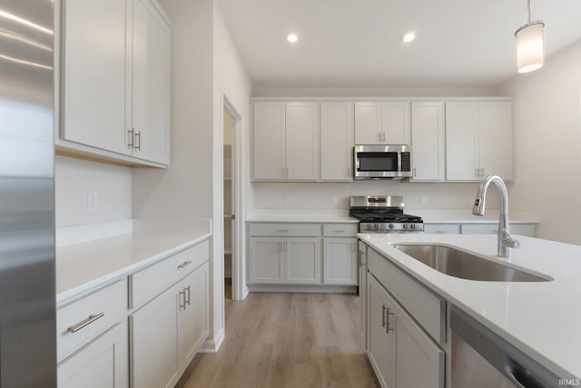 kitchen featuring white cabinets, hanging light fixtures, sink, light wood-type flooring, and appliances with stainless steel finishes