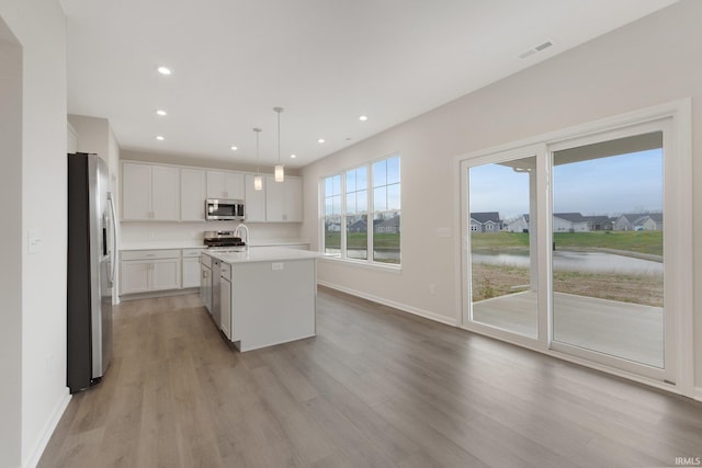 kitchen featuring a center island with sink, white cabinets, pendant lighting, light wood-type flooring, and appliances with stainless steel finishes