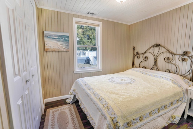 bedroom featuring ornamental molding, wood walls, dark hardwood / wood-style floors, and a closet