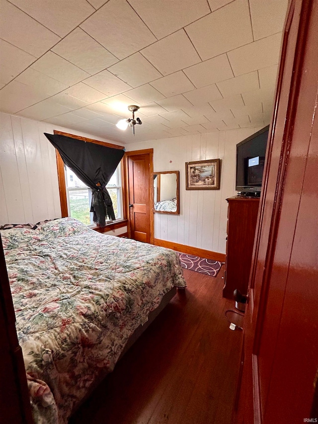 bedroom with dark wood-type flooring and wood walls