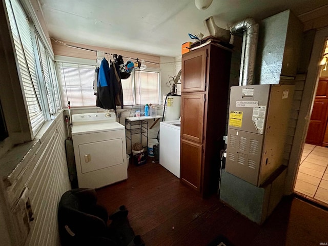 laundry room featuring washing machine and clothes dryer, hardwood / wood-style flooring, cabinets, and water heater