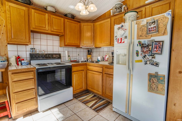 kitchen with light tile patterned floors, backsplash, white appliances, a notable chandelier, and tile counters