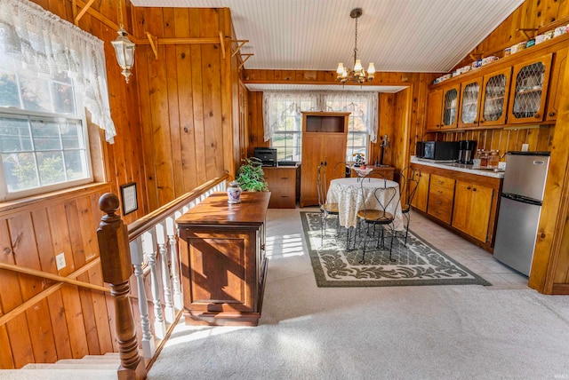 dining space featuring wood walls, light colored carpet, plenty of natural light, and vaulted ceiling