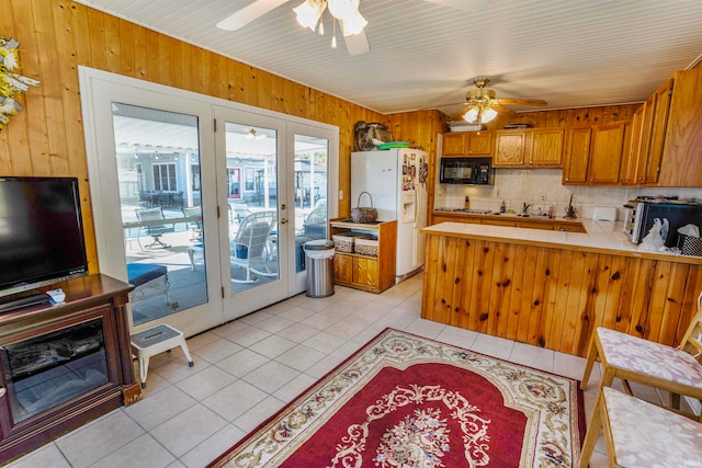 kitchen with tile countertops, tasteful backsplash, ceiling fan, white refrigerator with ice dispenser, and wooden walls