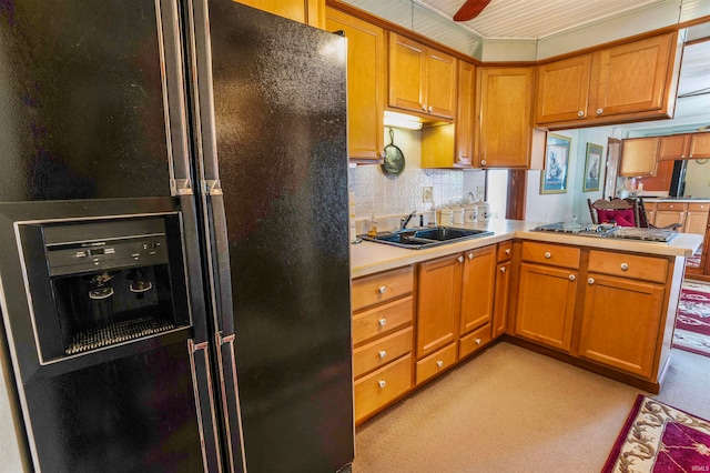 kitchen featuring stainless steel gas stovetop, kitchen peninsula, sink, black fridge with ice dispenser, and backsplash