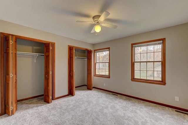 unfurnished bedroom featuring light carpet, ceiling fan, and two closets