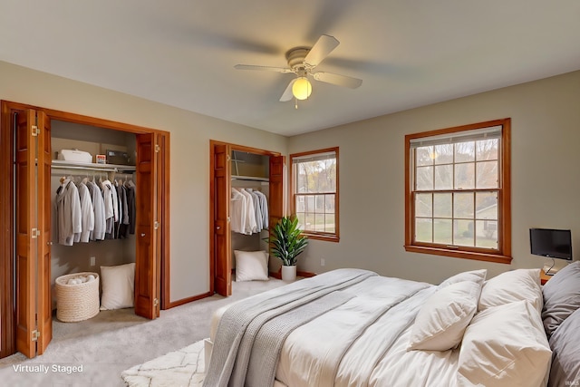 bedroom featuring light carpet, two closets, and ceiling fan