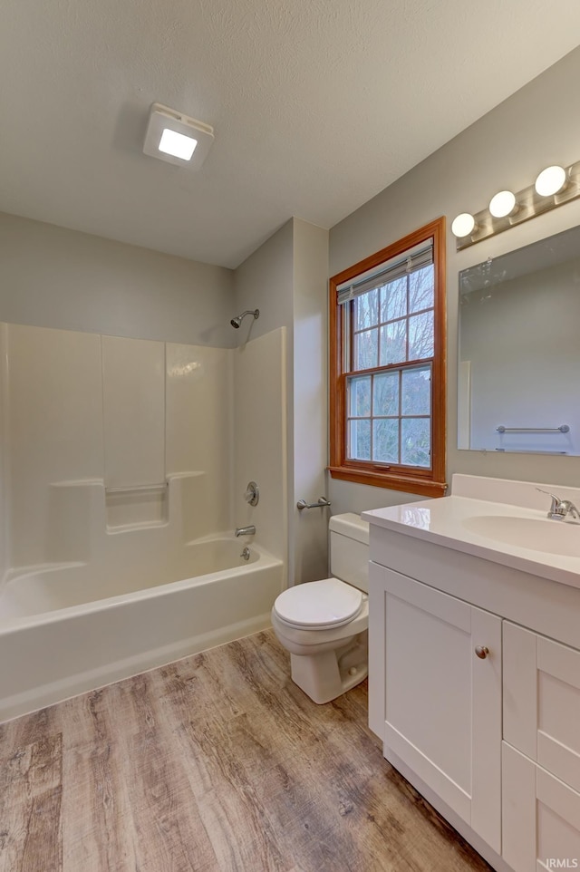 full bathroom with toilet, hardwood / wood-style floors, a textured ceiling, vanity, and bathtub / shower combination