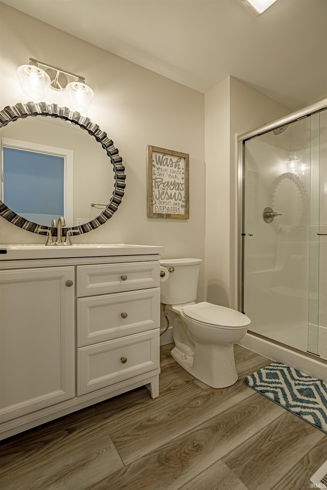 bathroom featuring wood-type flooring, vanity, toilet, and a shower with shower door