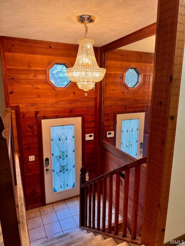 entryway featuring wood walls, a textured ceiling, a notable chandelier, and light tile patterned floors