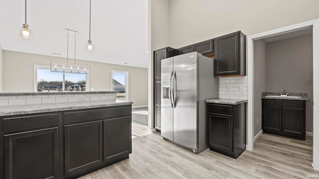 kitchen featuring decorative light fixtures, light stone counters, light hardwood / wood-style floors, decorative backsplash, and stainless steel fridge with ice dispenser