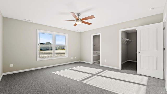 unfurnished bedroom featuring a closet, connected bathroom, carpet floors, a walk in closet, and ceiling fan