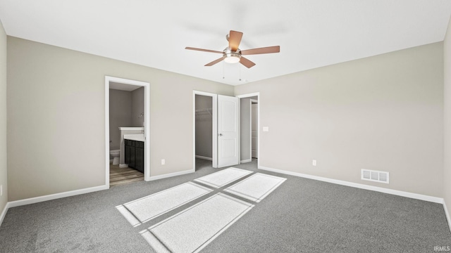 unfurnished bedroom with ceiling fan, a closet, carpet floors, a walk in closet, and ensuite bath