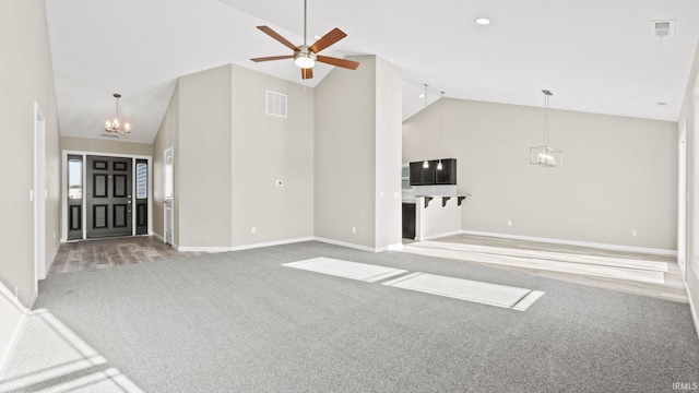 unfurnished living room with ceiling fan with notable chandelier, high vaulted ceiling, and carpet