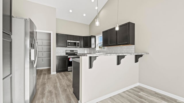 kitchen with a breakfast bar area, stainless steel appliances, hanging light fixtures, kitchen peninsula, and high vaulted ceiling